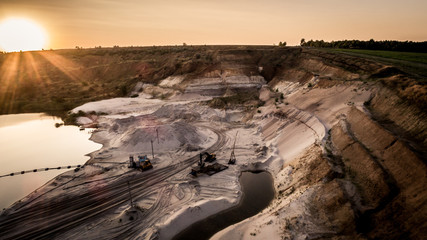 Aerial view of sandy quarry surface and mine equipment near lake at evening sunset