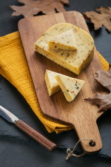 Cheese with herb in a cutting board on dark background.