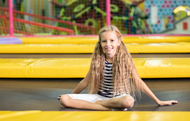 Little pretty smiling girl sitting on the  black-yellow trampoline