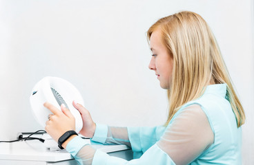 Teenage blond girl udergoes eye survey in ophthalmologic clinic holding diagnostics device