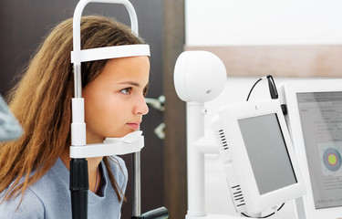 Teenage girl udergoing eye survey on modern diagnostics device in ophthalmologic clinic