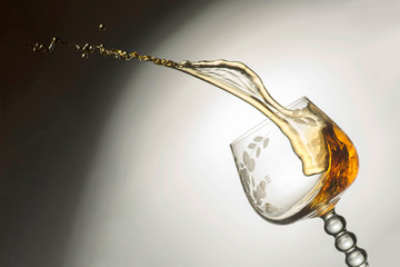Transparent glass with pouring whiskey, a jet of liquid up, clos