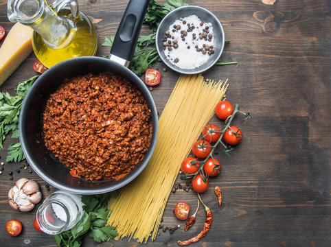 cooking tomato paste with minced meat, cherry tomatoes, parsley, onion and garlic, butter, tomato paste and cheese, the ingredients are laid out around the pan on a rustic wooden background