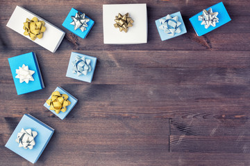 White and blue gift boxes decorated with gold and silver bows are arranged in the corner of the wooden background. Copy space. Festive layout.