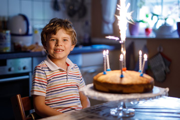 Adorable happy blond little kid boy celebrating his birthday. Child blowing candles on homemade...