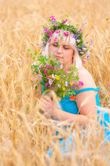 Beautiful young woman in wreath of wild flowers in wheat meadow on sunny day.