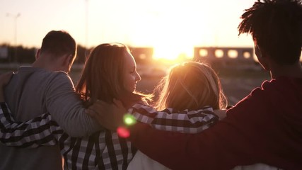 Group of friends walking embracing and having fun together in city. They are two girls and two boys in their twenties, friendship and lifestyle concepts, autumn clothing. Sun strongly shining on the - Powered by Adobe
