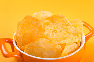 in an orange pan a lot of chips with spices, fast food concept, on yellow background