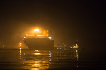 Large merchant container ship in port area during fog. A merchant ship is moving at container...