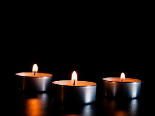 Three lighted candles with an orange flame and isolated on a black background