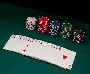 A deck of poker cards and poker chips of various colors on a green mat