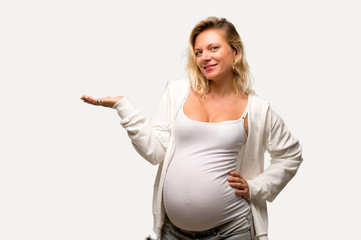 Pregnant blonde woman with white sweatshirt holding copyspace imaginary on the palm on isolated...