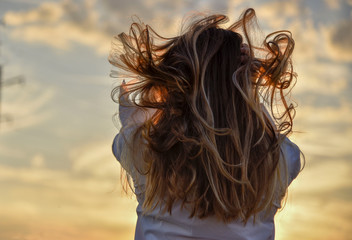 Girl with beautiful hair at sunset sitting on a haystack back to the photographer