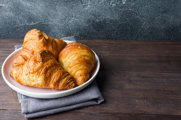 Freshly baked croissants on a plate, dark background, copy space.