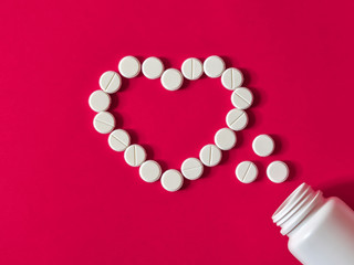 Medical white pills in heart symbol on pink background