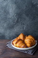 Freshly baked croissants on a plate, dark background, copy space.