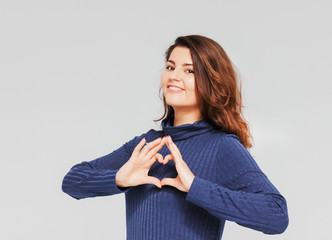 Fototapeta premium Beautiful romantic brunette girl making heart gesture with his h