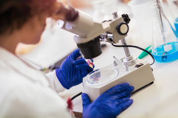 Woman scienist in laboratory. Young scientist looking through a microscope in a laboratory. Young scientist doing some research.