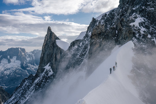 Climbers or alpinist on a knife sharp ridge of an alpine peak or summit of Aiguille du Rochefort. Alpine landscape and adventure climbing ascent in Mont Blanc Massif. Alpinism in high mountains.