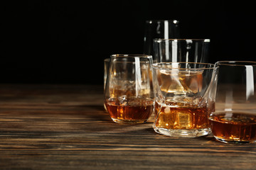 Glasses of whiskey on wooden table against black background