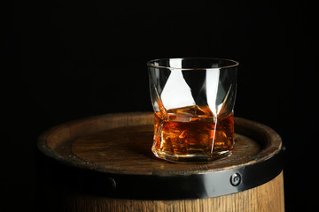 Glass of whiskey on wooden barrel against black background