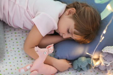Obraz na płótnie Canvas Cute little girl with toys sleeping in play tent