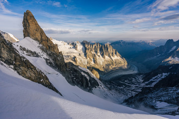 View of a high alpine landscape of Mont Blanc Massif, the Aiguilles du Chamonix and a glacier. Great alpine sunset light, snow, high rocks and summits and peaks. France and Italy.