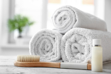 Rolled clean white towels, cosmetic and brush on table indoors