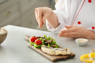Young female chef preparing tasty dish in kitchen, closeup