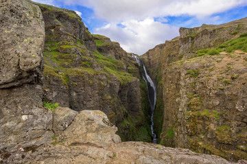 The Glymur Waterfall with golden clouds in the sky. The flowing water is captured by a long exposure. Amazing blue color of water from the glacier. Natural and colorful environment...