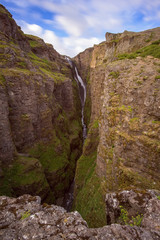 The Glymur Waterfall with golden clouds in the sky. The flowing water is captured by a long exposure. Amazing blue color of water from the glacier. Natural and colorful environment...