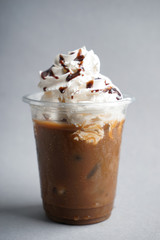 Cold coffee covered with whipped cream and chocolate in wet plastic cup on light background