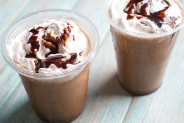 Cold coffee covered with whipped cream and chocolate in wet plastic cups on wooden table, closeup