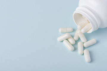 Pills with white powder in white plastic bottle on blue background with copy space