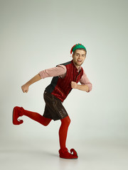 The happy smiling friendly man dressed like a funny gnome or elf running on an isolated gray studio...