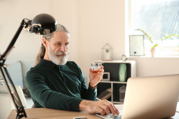 Senior man drinking whiskey while working on laptop at home