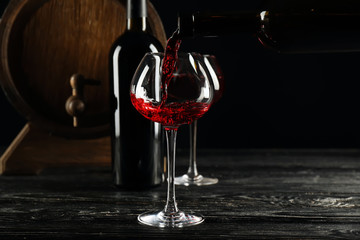 Pouring of wine from bottle into glass on dark background