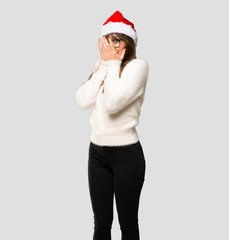 Girl with celebrating the christmas holidays covering eyes by hands and looking through the fingers on isolated grey background