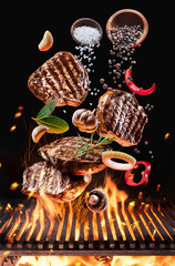 Grilled beef steaks with vegetables and spices fly over the glowing grill barbecue fire.