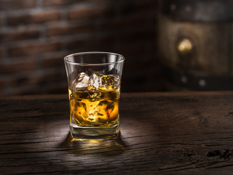 Whiskey glass or glass of whiskey with ice cubes on the wooden background.