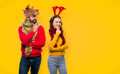 Couple dressed up for the christmas holidays looking to the side with the hand on the chin on yellow background