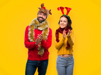 Couple dressed up for the christmas holidays applauding after presentation in a conference on yellow background