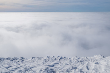 Mountain tops covered with snow above the white heavy clouds.