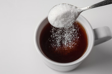 Pouring of sugar into cup of coffee on light background
