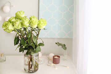 Vase with beautiful green roses on white table in room