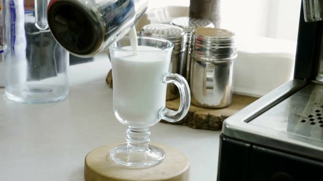 Making coffee. Close-up shot of barista pouring hot milk into a glass goblet. 4K