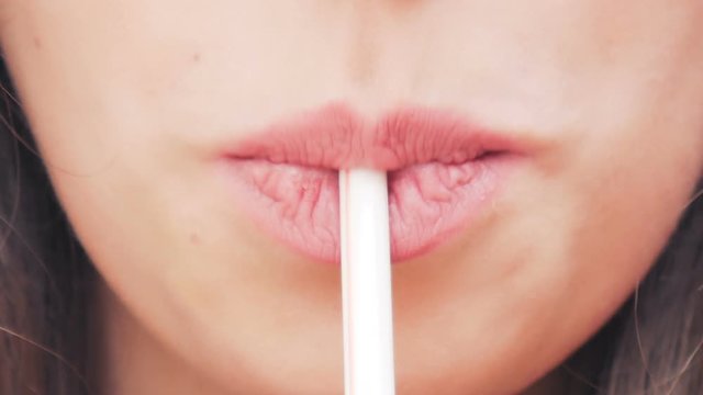 Young cute girl eagerly drinks a cocktail from the straw. Close up.