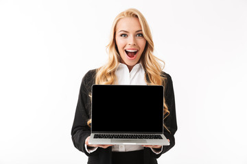 Photo of beautiful businesswoman wearing office suit smiling while holding laptop with black screen, isolated over white background in studio