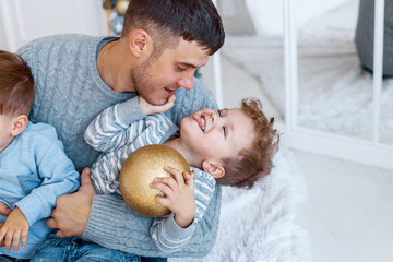 A daddy with his two sons twins in front of the christmas tree  with candles and gifts hugging and having fun. New year's eve. Cozy holiday at the fir-tree. love, happiness and big family concept