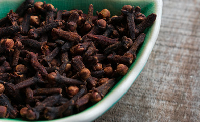 Cloves in small dish, on wooden background